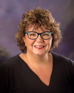 Caucasian female with wavy hair and thick black rimmed glasses