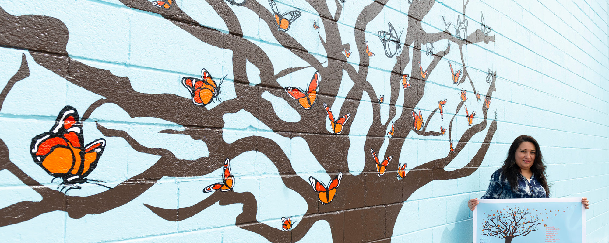 Image of student holding art next to her mural