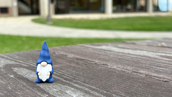 image of a blue gnome on a picnic table with Wyllie hall in the background