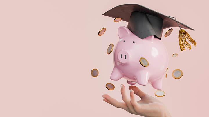 Decorative Hand holding pink piggy bank with graduation cap