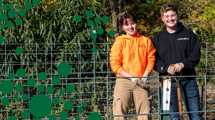 Two students in the Parkside gardens smiling at the camera, after taking a break from mulching