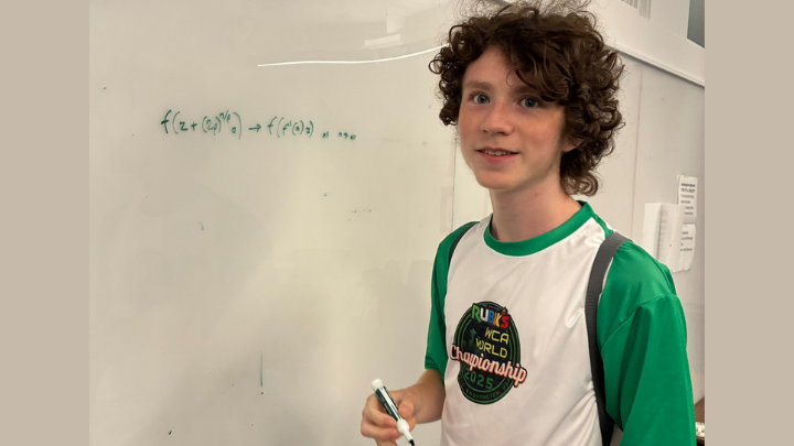 A young man stands in front of a whiteboard with a math equation on it.