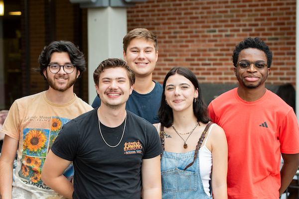 A group of five people smiling in front of a brick building.