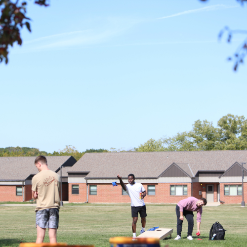 3 boys in on the terrace tossing bags. Bright blue sky.