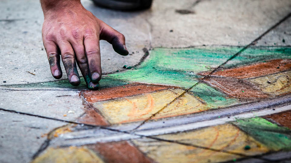 Man's hand creating chalk art on sidewalk