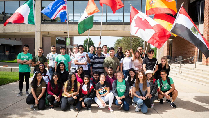 Image of a group of international student holding their counties flags, in front of the Parkside bridge