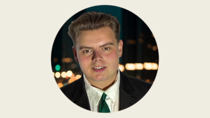A circular headshot of a young man in a black suit, white shirt, and green tie against a blurred nighttime city background with glowing lights.