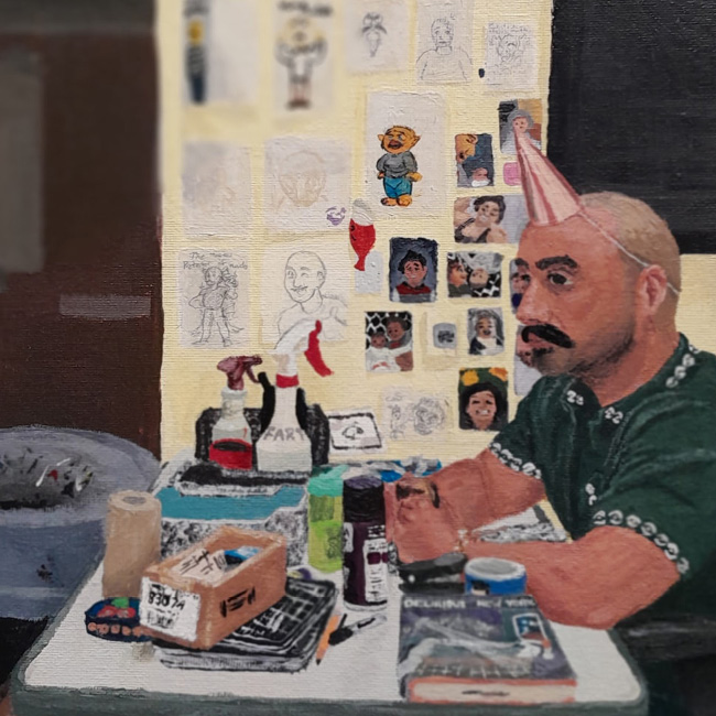 Image of man at desk with a party hat on and clutter on the table.