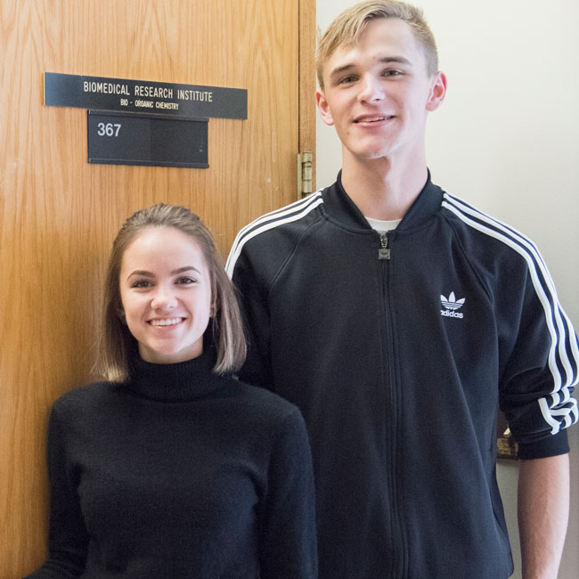 Sam Rozzoni and Mia Peterson standing in front of a door