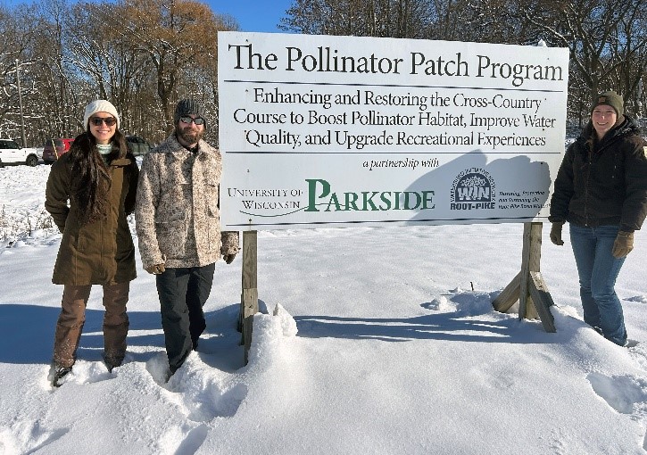 Group of people smiling with a sign promoting the Pollinator Patch