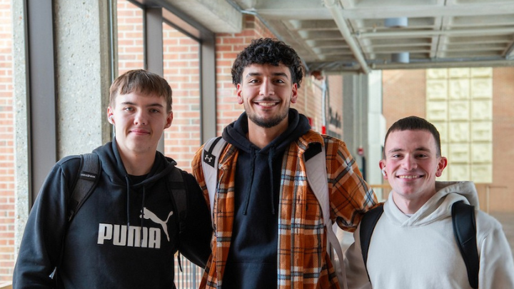 Three students smiling and standing together in a bright, modern campus hallway.