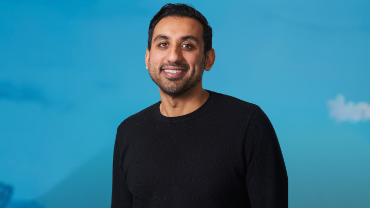 Ahmed 720x405 A man smiling in front of a blue background.