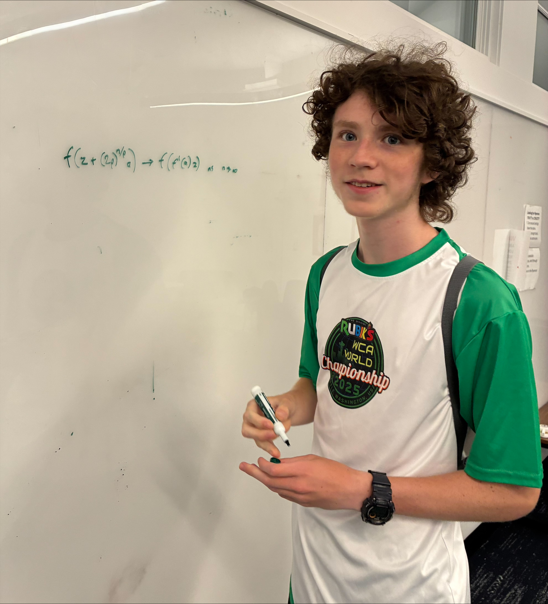 A young man stands in front of a whiteboard with a math equation on it.