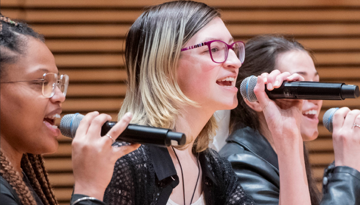 Three people singing into handheld wireless microphones