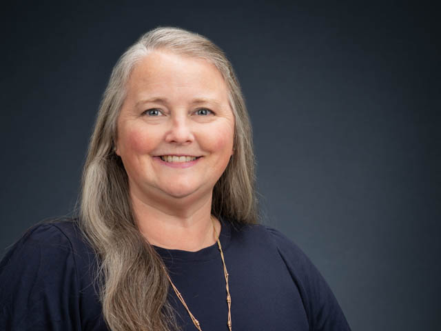 Photo of smiling woman with long, silver hair and a navy blue top. 