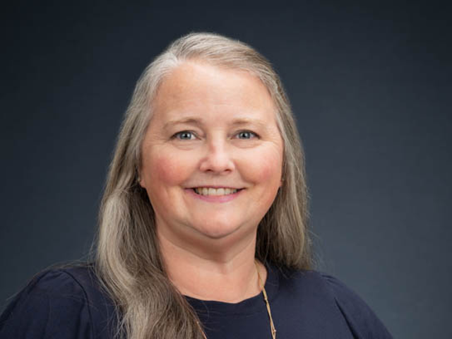 Photo of smiling woman with long, silver hair and a navy blue top. 