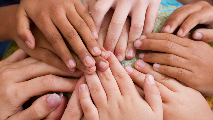 Image depicts many different hands coming together over a globe