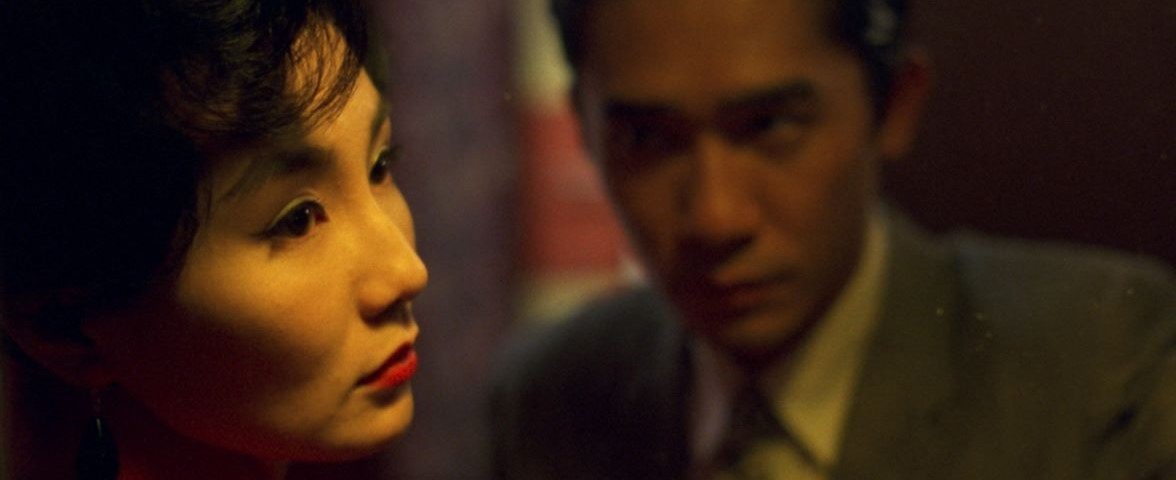 In the Mood for Love A woman looks off to the right and a man stands out of focus next to her staring at her