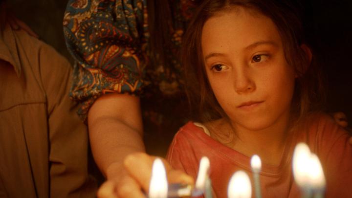 An adult lights candles on a birthday cake in front of a child