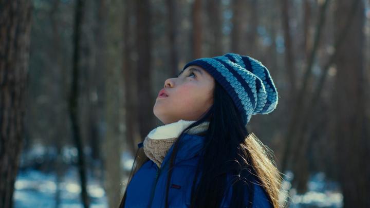 A child in a forest dressed up in winter clothes looking up