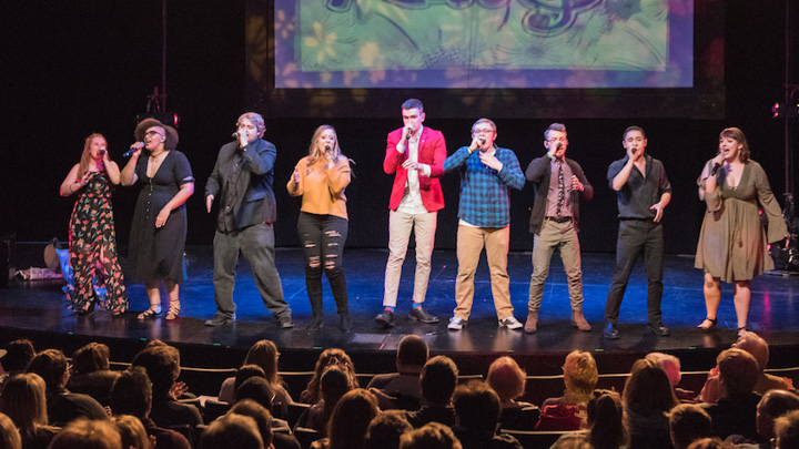 Students singing together on a stage with blue and orange lights