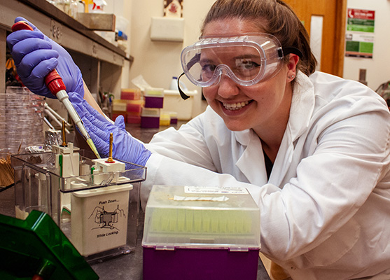 Brittany Dobrowski. Scientist smiling at camera while holding lab equipment.