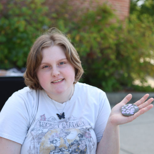 Girl outside wearing a white t-shirt holding a rock that says Zoe