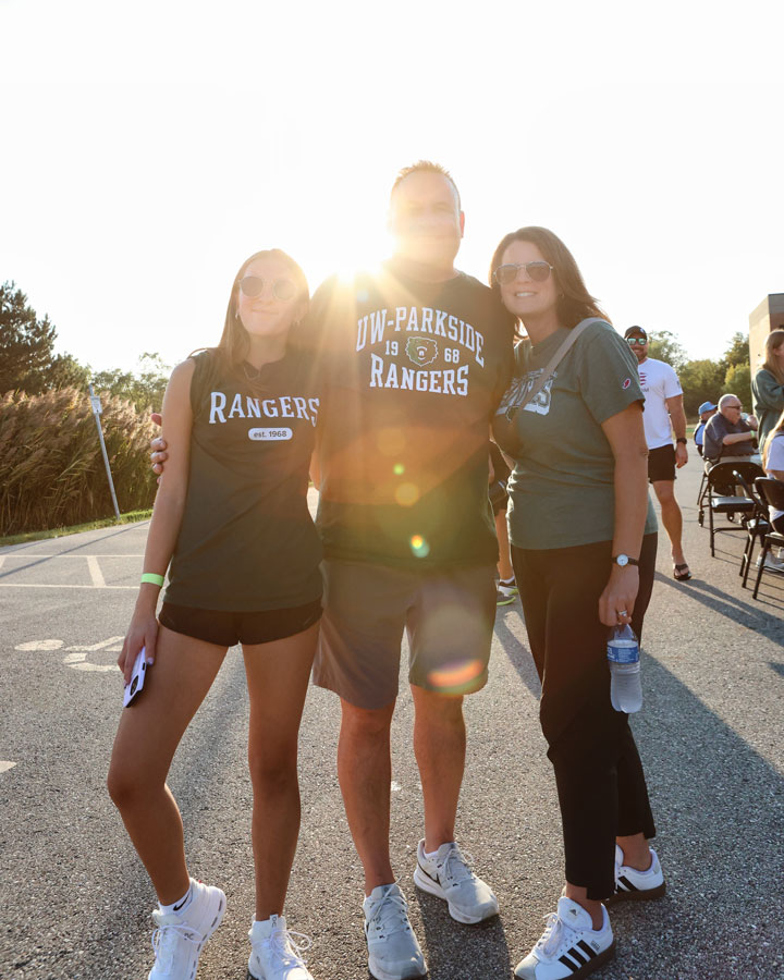 Three rangers at the homecoming tailgate posing together with the sun shining behind them.