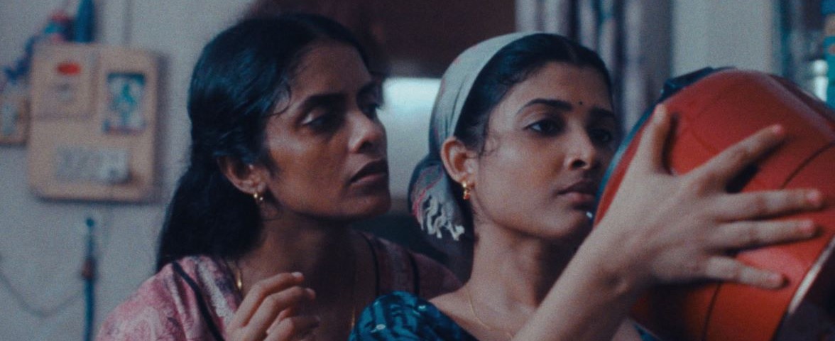 Two women, one standing behind the other, looking at an orange rice cooker
