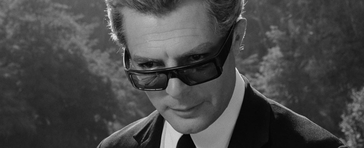 B&W image of a man holding a folded newspaper and looking down over sunglasses