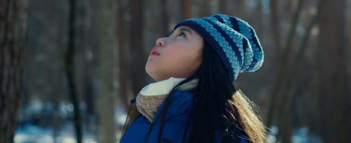 A child in a forest dressed up in winter clothes looking up