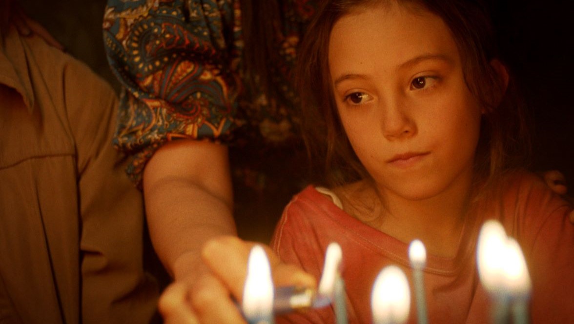 An adult lights candles on a birthday cake in front of a child