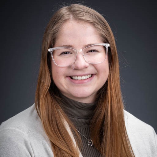 woman with brown hair and clear classes wearing a white cardigan and green long sleeves