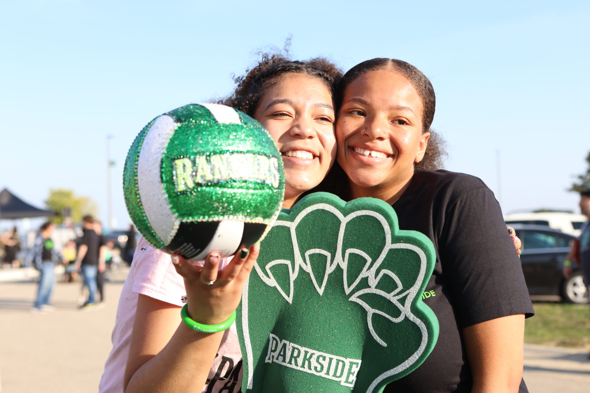 2 girls smiling. One is holding a volleyball and another is holding a Ranger Bear Claw.