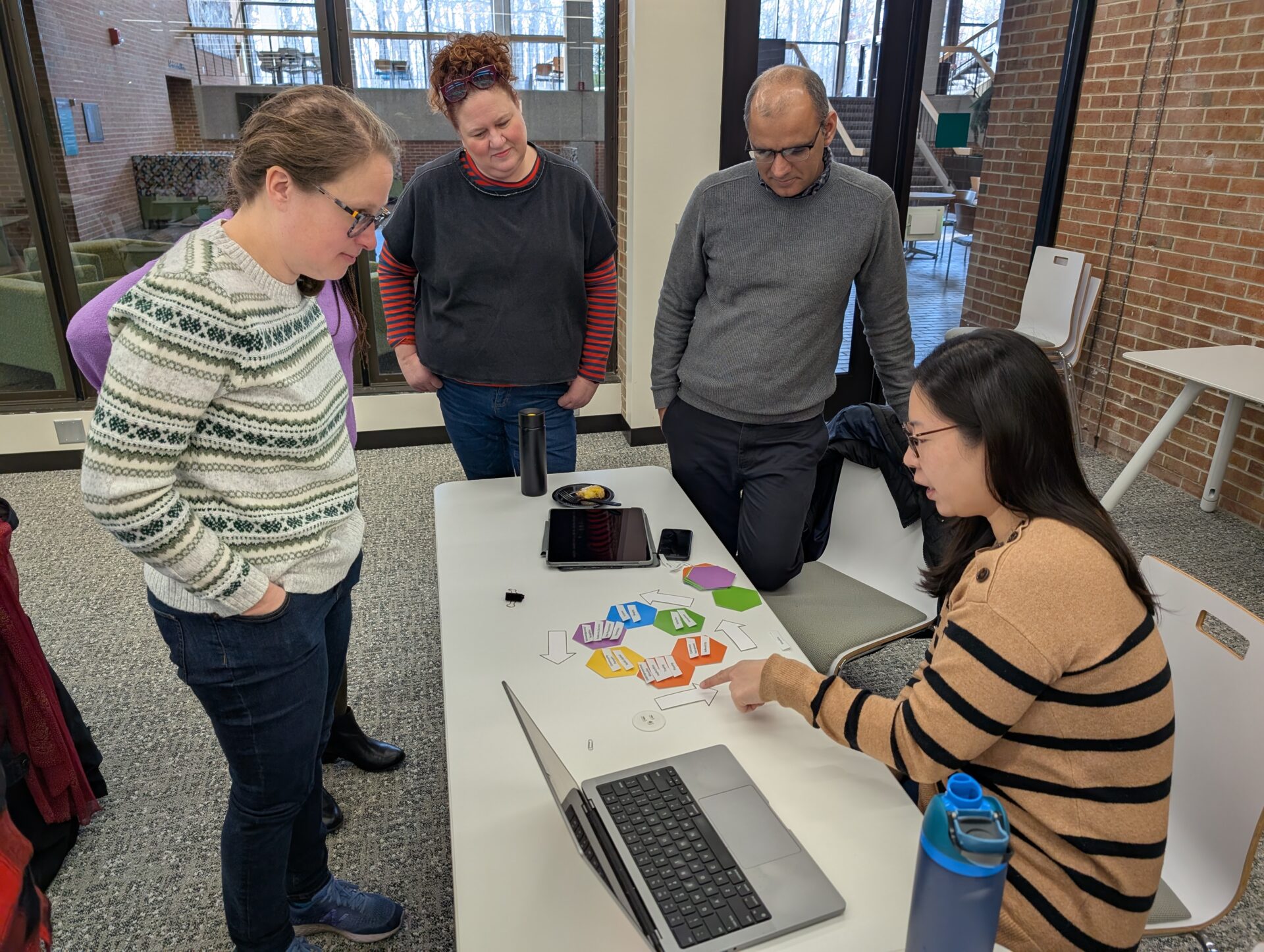 UW-Parkside faculty standing and sitting around a white table while doing a hexagonal thinking exercise together at a faculty development workshop