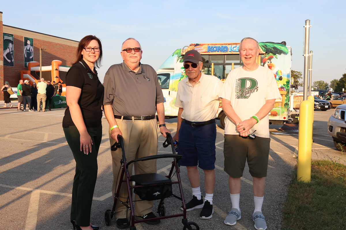Chancellor Akey standing with 3 alumni in the parking lot at sunset.